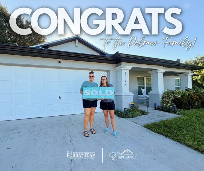 Couple holding a SOLD sign in front of their new home